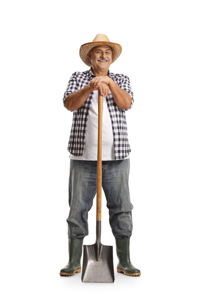 Full length portrait of a mature farmer leaning on a shovel and smiling isolated on white background - Foto, Imagem