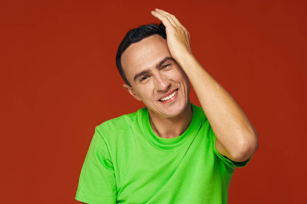 homme heureux dans un t-shirt vert touche sa tête avec sa main sur un fond rouge - Photo, image