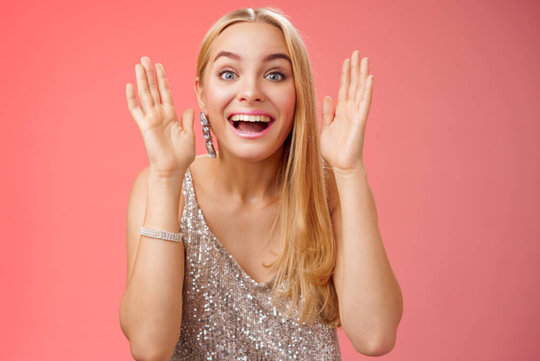 Impressed charming entertained blond european 25s woman in stylish silver glamour dress having fun playing peekaboo smiling joyfully hold palms near face laugh amused, standing red background - Photo, Image