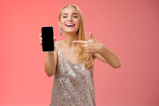 Opschepperige trotse elegante blonde vrouw in stijlvolle avondjurk show smartphone display trots wijzen mobiele telefoon scherm glimlachen tonen foto vriendje, staande rode achtergrond - Foto, afbeelding