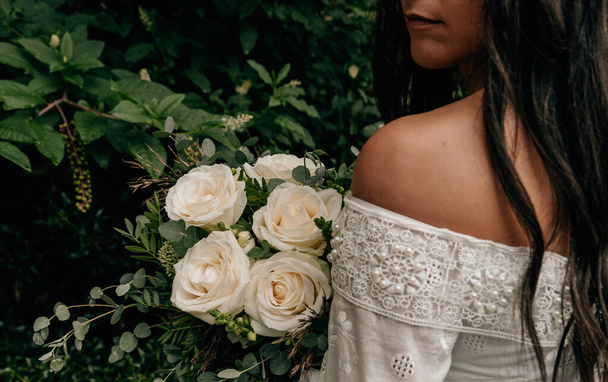 Close-up photo of bride wearing white wedding dress holding bouquet with white roses. - Photo, Image