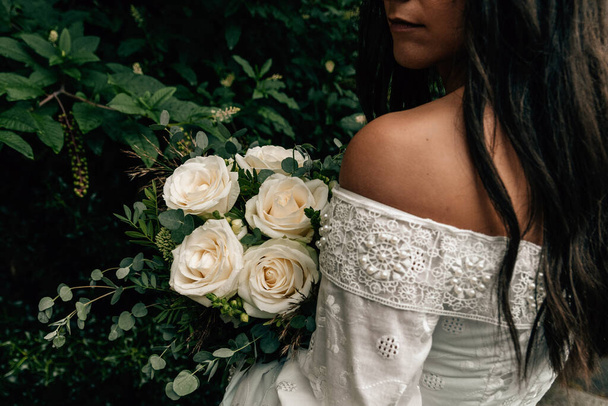 Close-up photo of bride wearing white wedding dress holding bouquet with white roses. - Photo, image