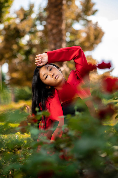 A portrait of an elegant East Asian woman wearing a red suit and posing in a garden in autumn in Spain - Fotoğraf, Görsel