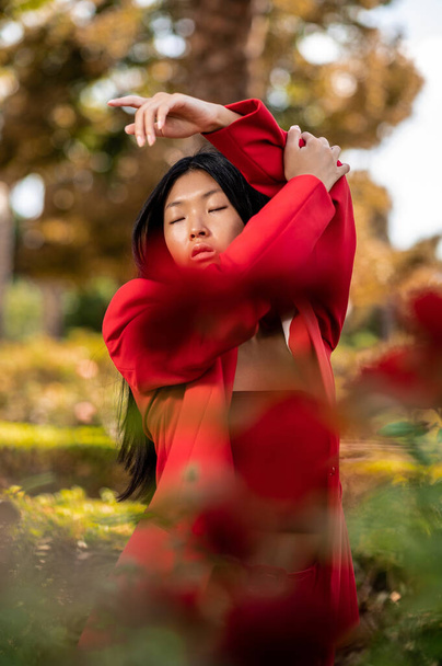 A portrait of an elegant East Asian woman wearing a red suit and posing in a garden in autumn in Spain - Foto, Bild