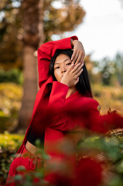 İspanya 'da sonbaharda kırmızı elbise giyen ve bir bahçede poz veren zarif bir Doğu Asyalı kadının portresi. - Fotoğraf, Görsel