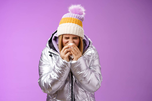 Meisje runny neus niezen weefsel pers servet gezicht ziek gevoel ziek rubriek ziekenhuis staande paarse achtergrond buigen het dragen van zilveren stijlvolle jas winter hoed, huilen snikken - Foto, afbeelding