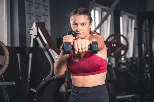 Una joven con pesas en el gimnasio. Retrato de mujer joven atractiva en ropa deportiva sosteniendo pesas haciendo ejercicio de fitness - Foto, Imagen