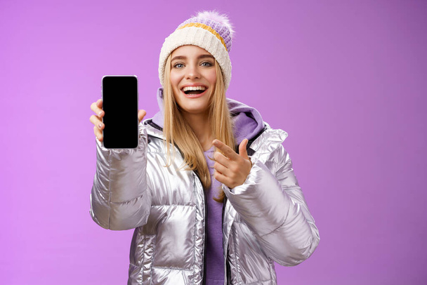 Tevreden geamuseerd goed uitziende blonde meisje suggereren neem kijkje smartphone display glimlachen gelukkig wijzen mobiele telefoon blij praten over geweldige nieuwe app functies, staande paarse achtergrond - Foto, afbeelding