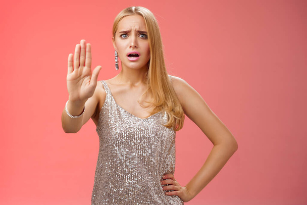 Freaked out displeased bothered insecure blond woman in silver glittering dress extend palm stop enough prohibition rejection gesture bothered pissed annoying clingy man nightclub, red background - Foto, afbeelding