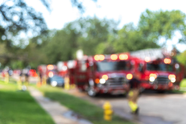 Розмитий пожежник ходить по вулиці і на тротуарі житлового будинку в передмістях Далласа, штат Техас, Америка. Ряд пожежних машин з драбинами і робочими пожежниками для концепції страхування від пожеж - Фото, зображення