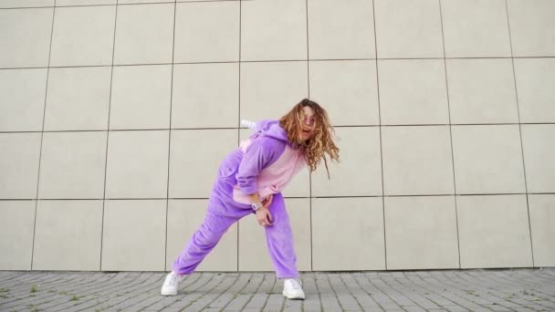 Funny cheerful happy young woman dancing outdoors on yellow wall. Crazy female hipster girl in a dress unicorn costume mask dance. Concept of fun people, happiness, joy Modern lifestyle in city street - Materiał filmowy, wideo