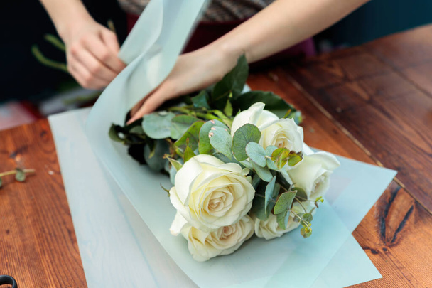 Mladá dospělá dívka květinářka dělá kytici bílých růží. Fotografie z blízka. - Fotografie, Obrázek