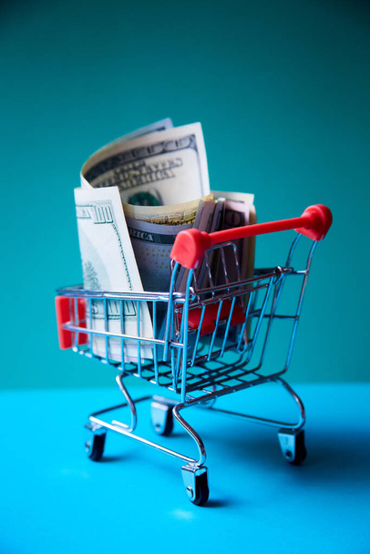 concept - curled dollar banknotes fall out of Shopping Cart Trolley against the green background - Foto, immagini
