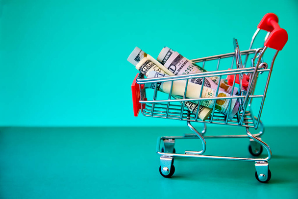 concept - curled dollar banknotes in Shopping Cart Trolley against the green background - Foto, Imagem