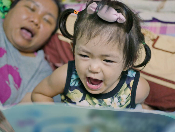 Una bambina, 2 anni, che legge ad alta voce, ripetendo dopo la zia, una favola della buonanotte - Foto, immagini