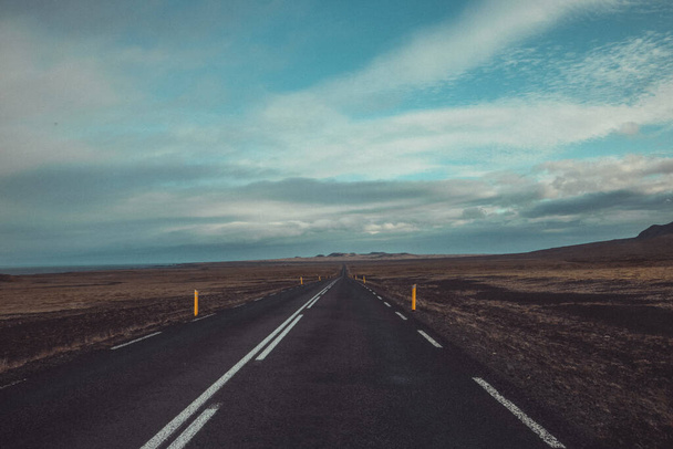 İzlanda 'daki asfalt yolun harika manzarası, dağlara doğru gidiyor. Issız dağlara doğru yol alan çizgiler ve yukarıdaki kalın bulutlar.. - Fotoğraf, Görsel