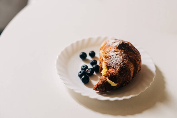 Круасан з вершками та чорницею на білій тарілці, концепція європейського сніданку
 - Фото, зображення