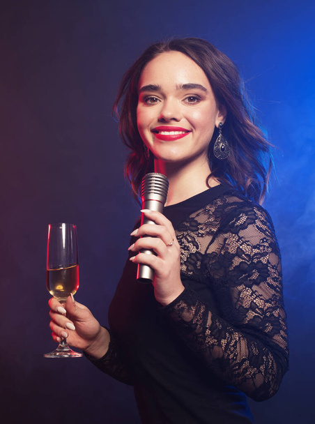 若い幸せな女性がパーティーでマイクに歌い、青い背景の上に写真. - 写真・画像