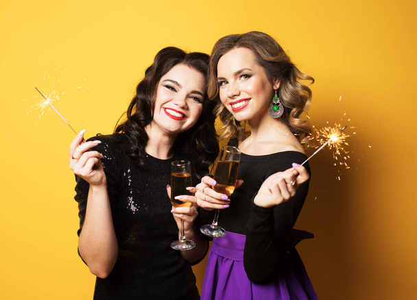 Két fiatal, divatos nő portréja pezsgős poharakkal és csillagszórókkal. - Fotó, kép