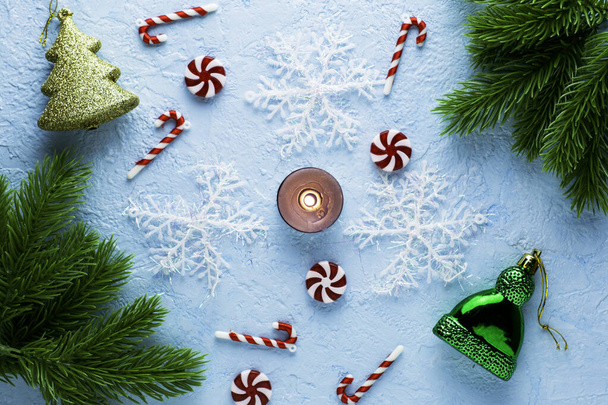 Πρωτοχρονιάτικο Χριστουγεννιάτικο φόντο σε μια μπλε επιφάνεια έλατα κλαδιά νιφάδες χιονιού καραμέλες ένα κερί καύση και διακοσμήσεις. Υψηλής ποιότητας φωτογραφία - Φωτογραφία, εικόνα