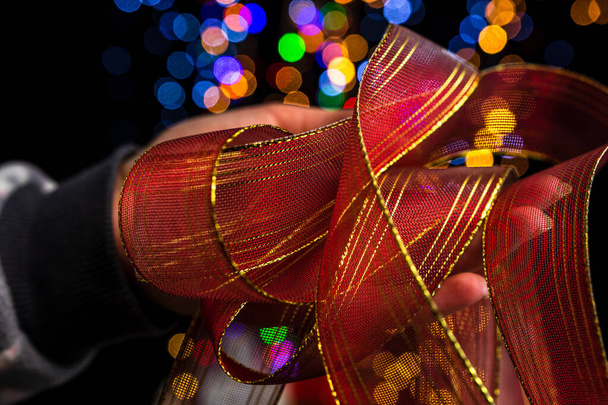 Un primo piano della mano tenendo il nastro di Natale contro bokeh luci sfondo. - Foto, immagini