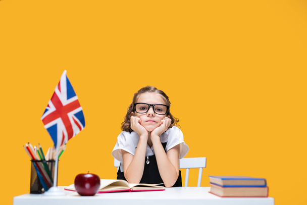 Sad boring caucasian schoolgirl in glasses studying at home. English lesson. Great Britain flag - Photo, Image