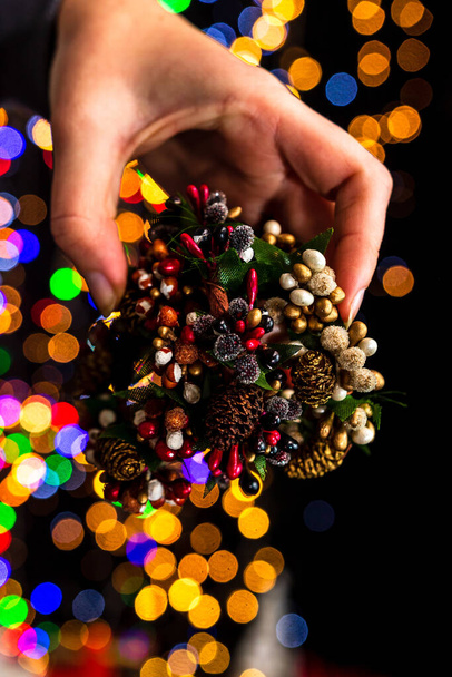 A vertical closeup of the hand holding Christmas decoration against bokeh lights background. - Foto, afbeelding