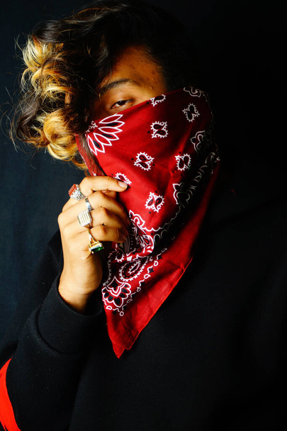 A closeup of a stylish Indian male wearing a red bandana over his face posing on the dark background - Foto, Imagem