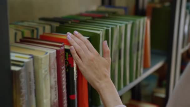 Close-up van een studente in een boek kiezen in de bibliotheek op een boekenplank. - Video
