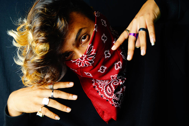 A closeup of a stylish Indian male wearing a red bandana over his face posing on the dark background - Photo, image
