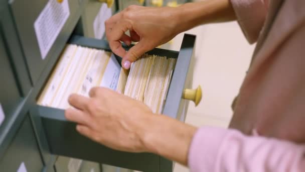 Ένα γυναικείο χέρι που ψάχνει κάρτες σε παλιό κατάλογο ξύλινη κάρτα. Ένας vintage κατάλογος βιβλιοθήκης, για μια βολική και γρήγορη αναζήτηση ενός βιβλίου. Αναζήτηση πληροφοριών στο αρχείο της κάρτας στη βιβλιοθήκη. - Πλάνα, βίντεο