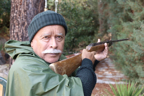 森の中のライフルを持つハンサムなシニアハンターのクローズアップポートレート - 写真・画像