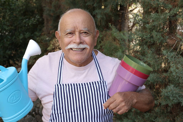 close-up portrait of handsome senior man with watering jug and plastic pots in garden - Фото, зображення