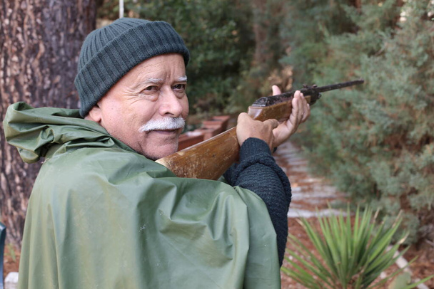 森の中のライフルを持つハンサムなシニアハンターのクローズアップポートレート - 写真・画像
