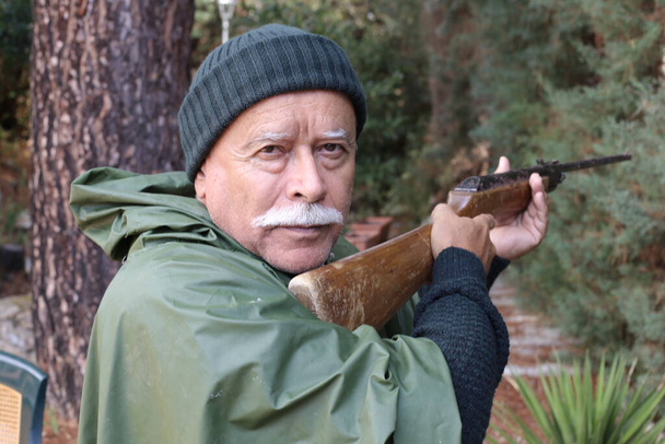κοντινό πορτραίτο όμορφου ανώτερου κυνηγού με τουφέκι στο δάσος - Φωτογραφία, εικόνα