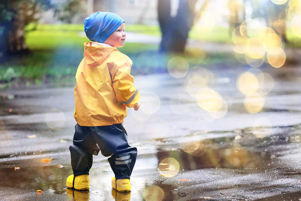 boy playing outdoors in puddles, autumn childhood rubber shoes raincoat yellow - Фото, зображення