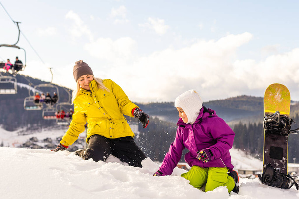 Mother and daughter with snowboards are playing in the snow - Photo, Image
