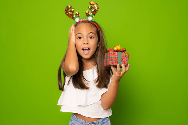 Boldog kis mosolygós lány télapó kalapban karácsonyi ajándékdobozzal. - Fotó, kép
