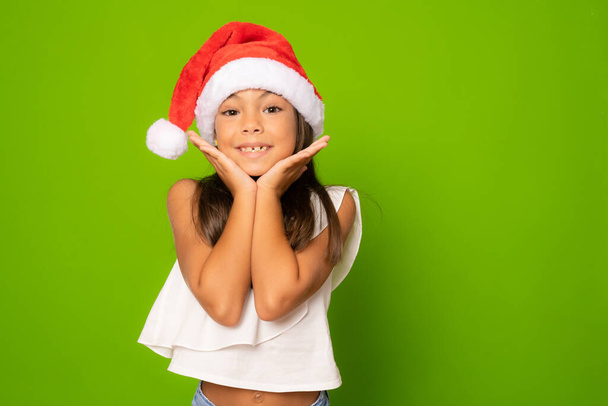 Happy little girl in santa hat isolated over green background. - Photo, Image