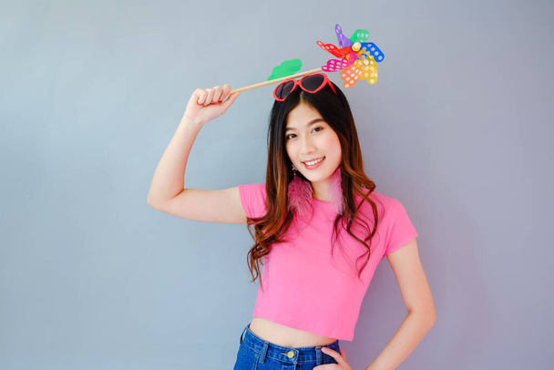 Portrait beautiful asian teen girl wearing pink dress on gray background, fashion summer set with colorful wind turbine or pinwheel or wind toy holding in hand,  emotions action, happy life concept - Fotoğraf, Görsel