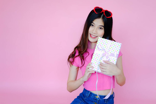 Portrait beautiful asian girl on pink background, model holding present in hand - Фото, изображение