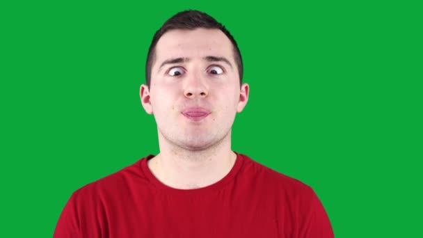 man grimaces at the camera while standing against the background of a green chroma key - Footage, Video