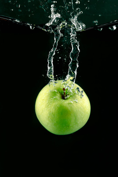 An apple in the water on a dark background - Foto, afbeelding