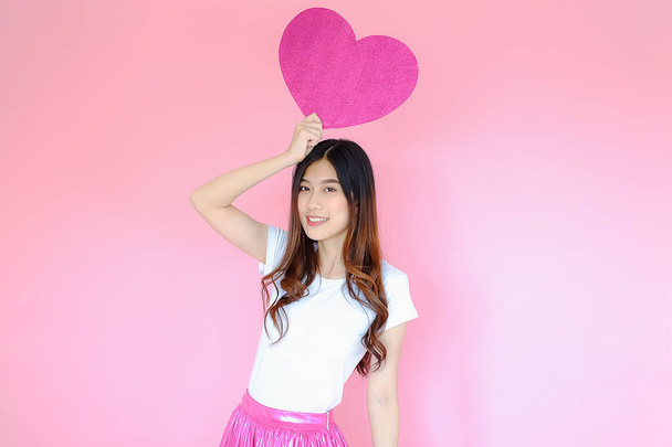 Portrait schöne asiatische Teenie-Mädchen tragen weißes T-Shirt und rosa Rock auf rosa Hintergrund, glücklicher Valentinstag in der Liebe Konzept, Modell hält rotes Herzschild in der Hand - Foto, Bild
