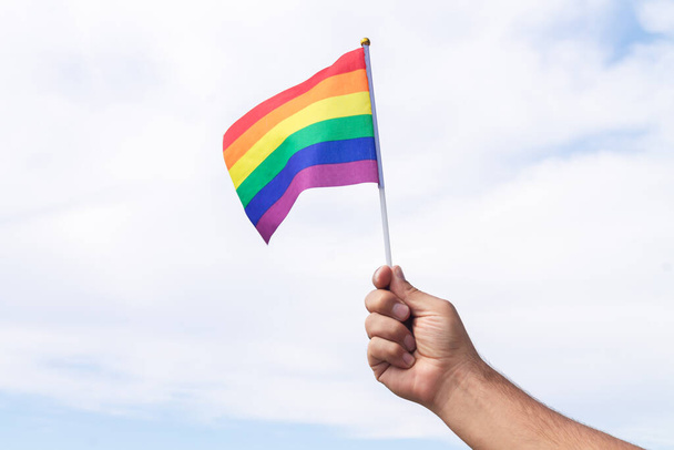 Człowiek trzyma gej dumy symbol tęczy flaga na tle nieba. Związki osób tej samej płci i koncepcja homoseksualizmu - Zdjęcie, obraz