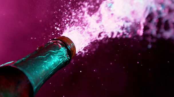 Champagne explosion, freeze motion of flying wine splashes. Neon lights. Celebrating concept, happy New Year theme. - Photo, image
