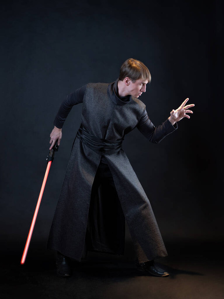 A villain with a red lightsaber, a young man in a long robe does fighting poses, - Valokuva, kuva