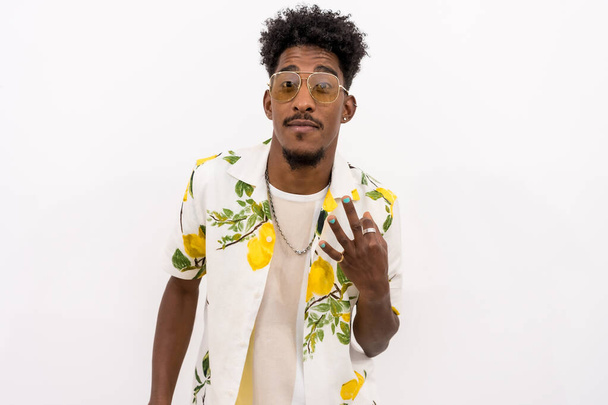 A young Cuban man in a floral shirt and glasses smiling and dancing on a white background, copy and paste space - Foto, imagen