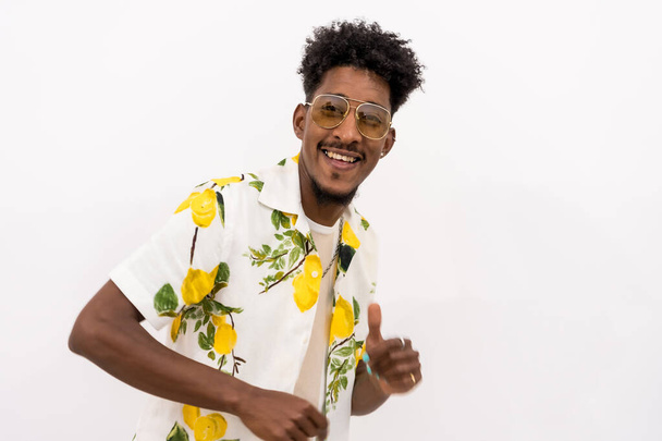 A young Cuban man with a white and green flower shirt, glasses, smiling and dancing on a white background, copy space and paste - Foto, Bild