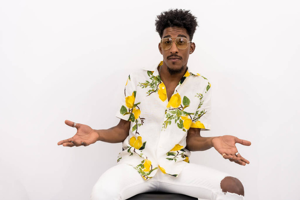 A young Cuban man with curly hair sitting in a white flowered shirt and glasses. Shocked or embarrassed looking at camera on a white background - Fotoğraf, Görsel